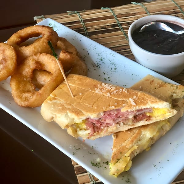 Cuban sandwich with ham, cheese, and pickles, served with onion rings and black bean soup.