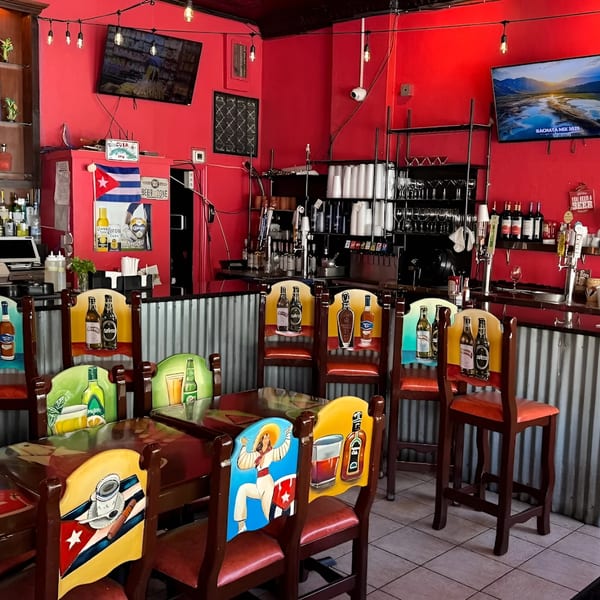 Interior of Las Palmas Restaurant with red walls, bar area, and colorful chairs depicting Cuban themes.