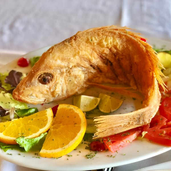 Whole fried fish with crispy skin, garnished with orange slices, lime wedges, and tomatoes.