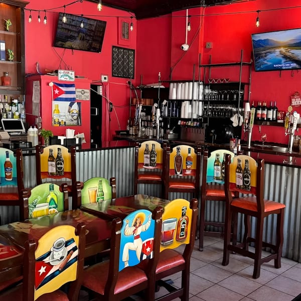 Interior of Las Palmas Restaurant with red walls, a bar, and chairs with colorful Cuban-themed paintings.