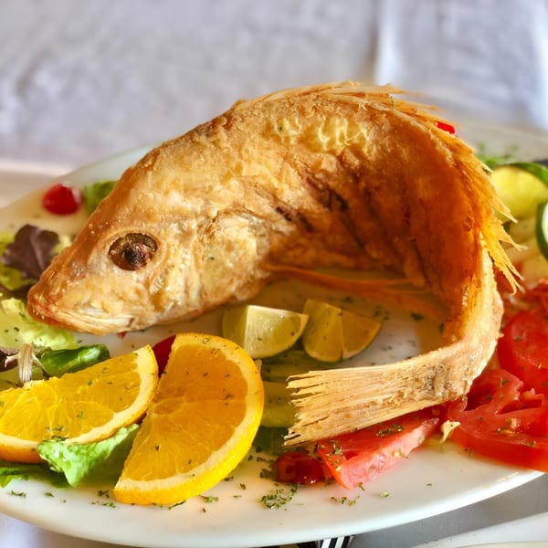 Whole fried fish with crispy skin, garnished with orange slices, lime wedges, and tomatoes.