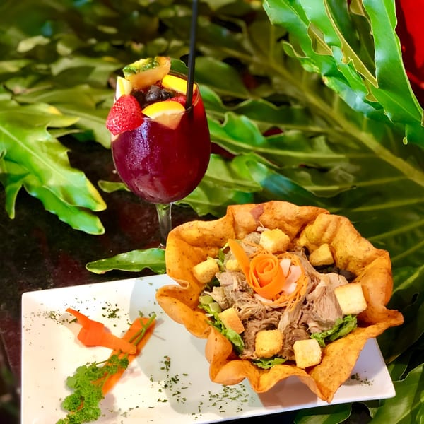 A vibrant red sangria and a Cuban pork salad in a crispy tortilla bowl on a white plate.