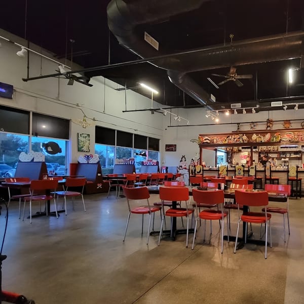 Interior of Las Palmas Restaurant with red chairs, dark tables, and a bar area with Cuban-themed decor.