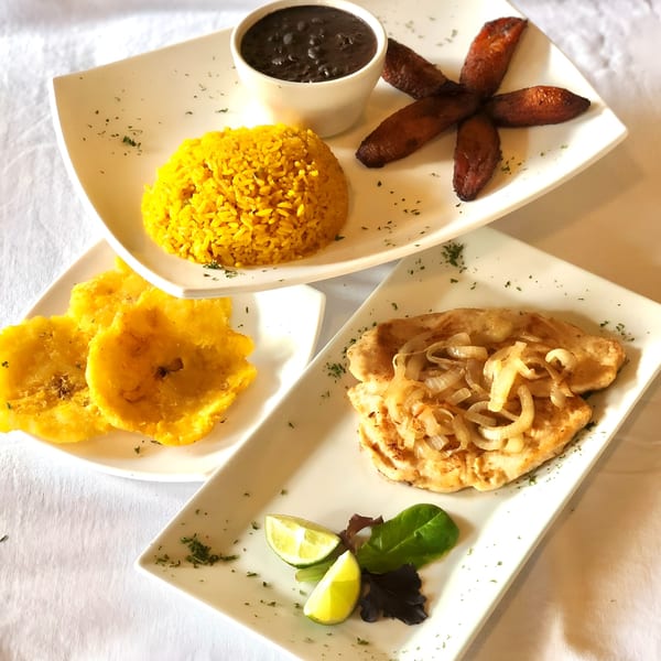 Cuban dishes: yellow rice, black beans, fried plantains, and chicken with onions, on white plates.