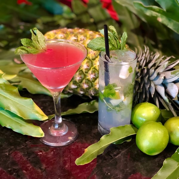 Two refreshing Cuban cocktails, a red martini and a mojito, with pineapples and limes.