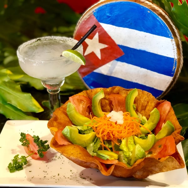 A Cuban salad in a fried tortilla bowl with a margarita and a Cuban flag drum in the background.