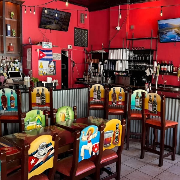 Colorful Cuban-themed chairs and tables in a vibrant red restaurant interior with a bar.