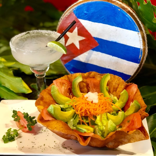 A fresh salad in a crispy tortilla bowl with a margarita and a Cuban flag in the background.