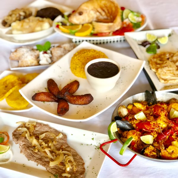 A table laden with various Cuban dishes, including steak, paella, plantains, and desserts.